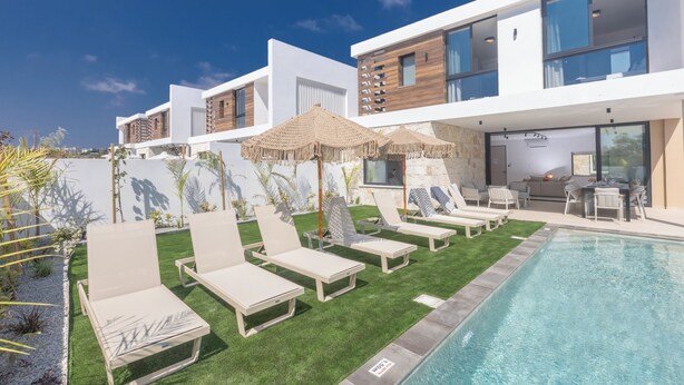 A modern hotel with a pool, lounge chairs, and a dining area. - Ayia Napa Orea Villa OR2 (Ayia Napa)