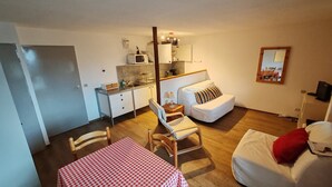 A compact room with a kitchenette, a dining area with a checkered table, a sofa with a striped pillow, and a bed with a red pillow. - Studio in Les Deux Alpes near Ski Slopes (Les 2 Alpes)