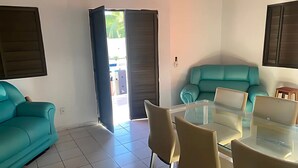 A modern living room with teal sofas, a glass dining table, and a sliding door leading to an outdoor area. - BSM Beach House - Top Leisure! (Barra Mar Barra de São Miguel)