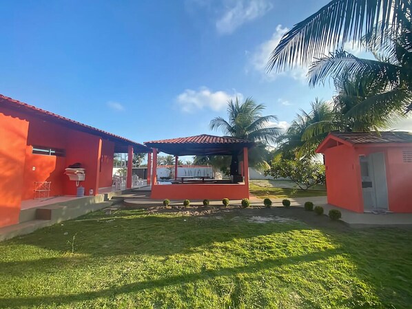 A courtyard with a covered seating area, surrounded by red buildings and palm trees.