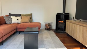 A modern living room with a sofa, a coffee table, a TV, and a wood-burning stove. - Rainforest retreat near Canyon Lookout & trails, mins to Springbrook wonders (Springbrook)