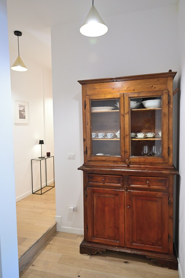A wooden cabinet with glass doors, a small table with a lamp, and a wooden floor.