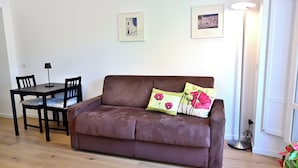 A brown leather sofa with floral cushions, a small table with chairs, and two framed artworks on the wall. - At Home Colosseo (Rome)