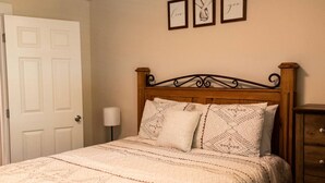 A neatly made bed with a patterned bedspread and pillows, a wooden headboard, a bedside lamp, and a dresser with drawers.