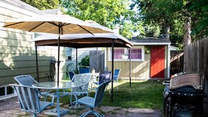 A patio with a glass table and chairs, a covered umbrella, and a barbecue grill.