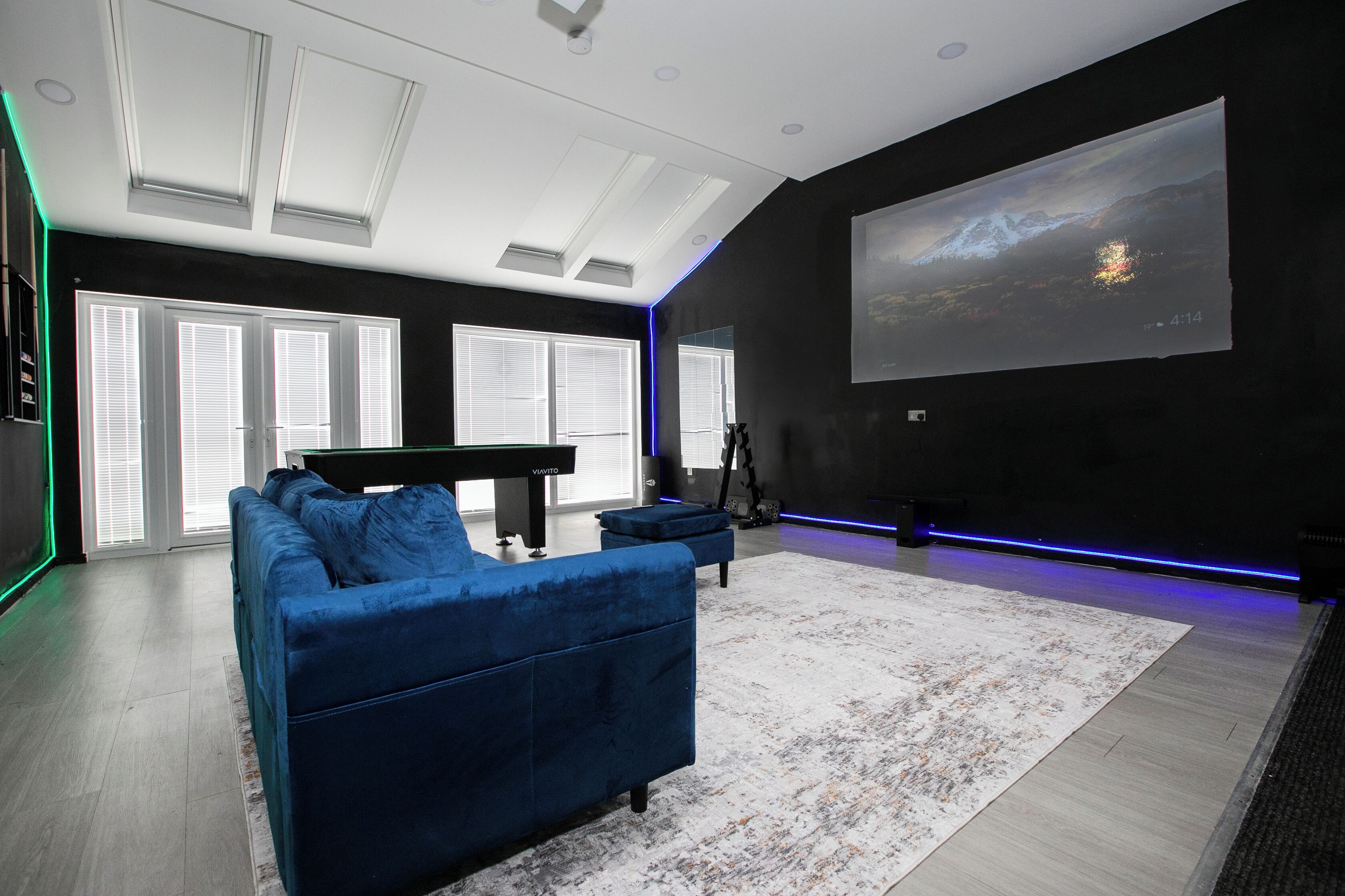Een moderne woonkamer met een blauwe bank, een piano en een groot scherm waarop een berglandschap staat.