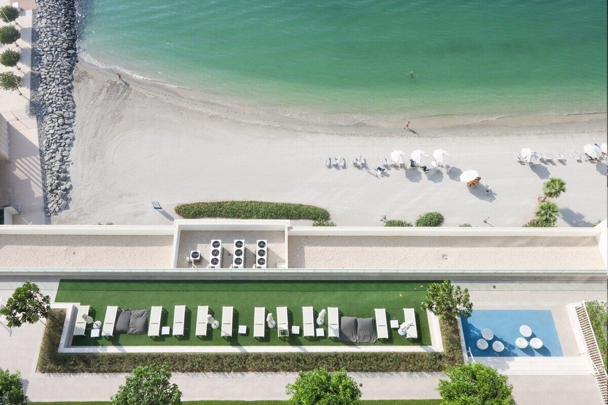 An aerial view of a beachside hotel with a pool area, beach chairs, and umbrellas.