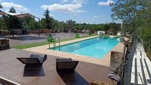 A rectangular swimming pool with a tiled deck, surrounded by lounge chairs and a covered seating area.