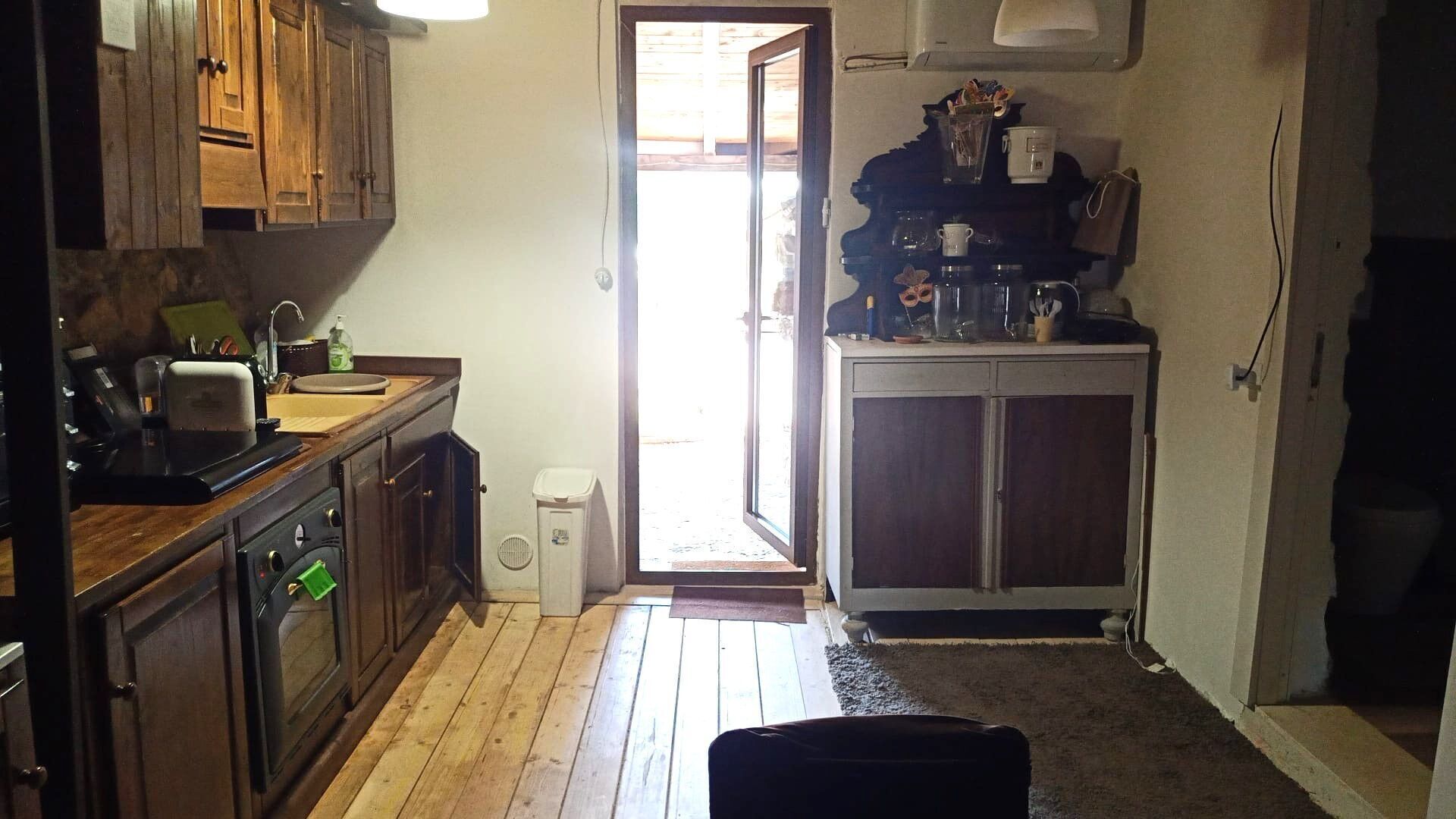A compact kitchen with wooden cabinets, a countertop with various appliances, and a door leading to a bright outdoor area.