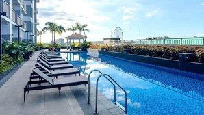 A swimming pool with lounge chairs, a Ferris wheel, and a building in the background. - COAST RESIDENCE (Pasay)