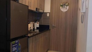 A compact kitchen with wooden cabinets, a black refrigerator, and a tiled floor. - COAST RESIDENCE (Pasay)