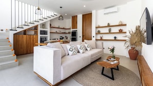 Un salon moderne avec un escalier, un canapé, une table basse et un coin cuisine en arrière-plan.