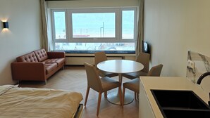 Habitació d'hotel amb llit, sofà, taula de menjador amb cadires, televisió i finestra gran amb vista a la platja.