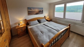 Een slaapkamer met een houten bed, twee nachtkastjes, een raam met jaloezieën, en een schilderij aan de muur.