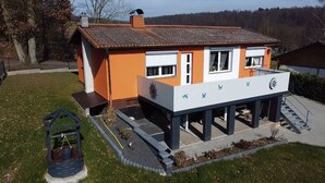 Een huis met een verhoogd terras, een kleine tuin en een vogelhuisje.