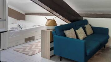 Ein gemütliches Schlafzimmer mit einem Etagenbett, einem blauen Schlafsofa und einem gewebten Korb auf einem Nachttisch aus Holz.