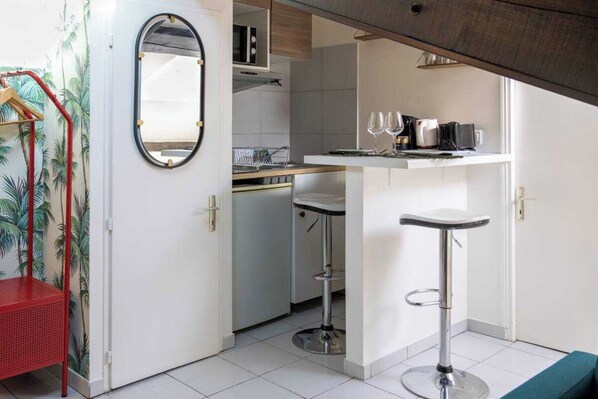 A compact kitchen with a bar area, a red chair, and a mirror.