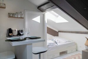 A bedroom with a skylight, a bed, a bedside table with a glass of wine, and a small seating area.