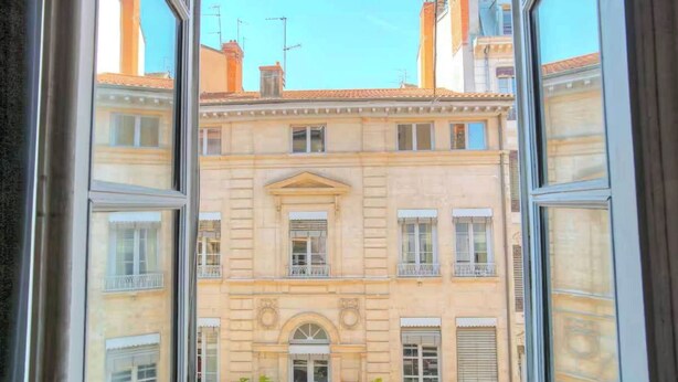 A view through a window of a building with a central arched window and multiple balconies. - Dify Apartment Ainay (Lyon)