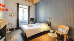 A bedroom with a bed, bedside table, lamp, chair, and a window with curtains. - Dify Apartment Ainay (Lyon)
