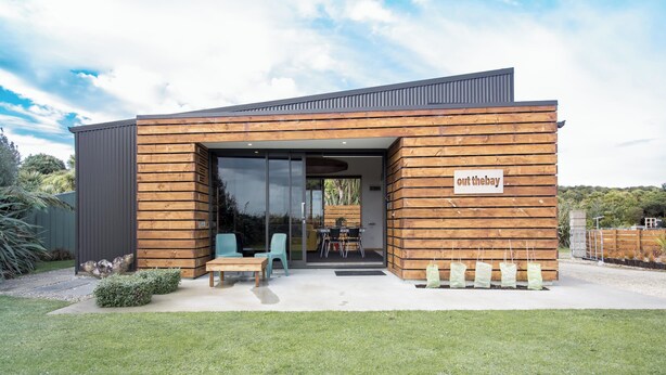 A modern building with a wooden facade, a sign reading "out the bay," and a patio area with outdoor seating.