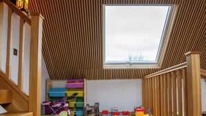 A spacious room with a high ceiling, a skylight, a play area with toys, and a patterned carpet.