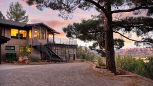 A modern house with a brick driveway, a staircase leading to a deck, and a view of red rock formations.