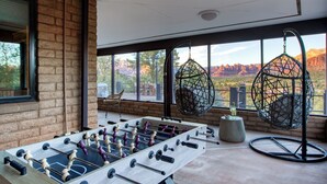 A foosball table in a room with large windows overlooking a canyon, a hanging chair, and a modern light fixture.