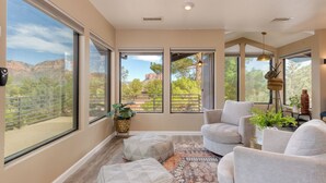 A spacious room with large windows offering views of a mountainous landscape. There are two white armchairs and a patterned rug on the floor.
