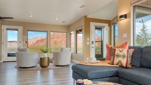A spacious living room with a large sofa, two armchairs, a coffee table, and a view of red rock formations through large windows.
