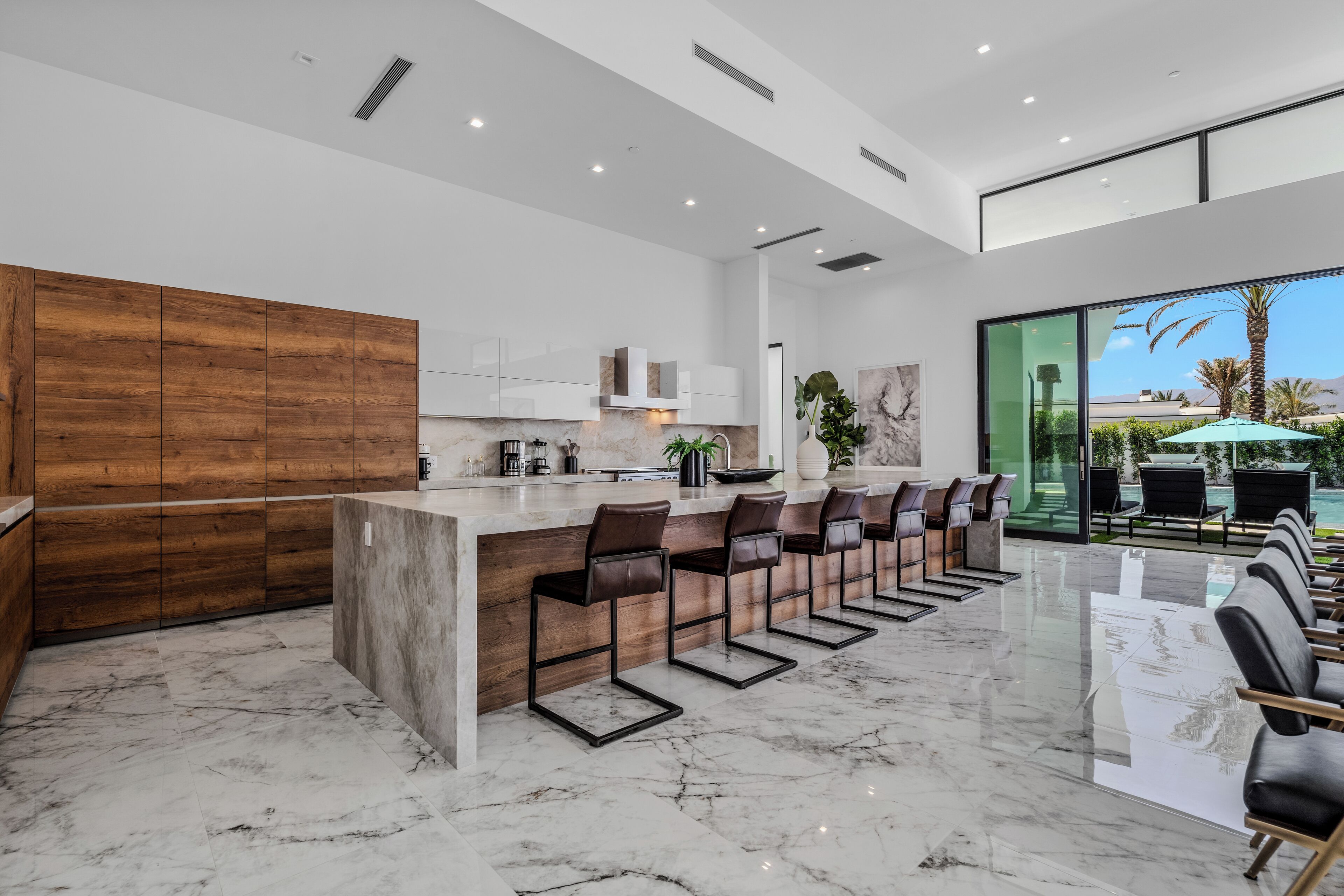 A modern kitchen with a marble countertop, wooden cabinets, and a bar area with bar stools.