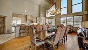 A spacious dining area with a large wooden table and patterned chairs, a chandelier, and a view of the kitchen and windows. - 7 Condos, Ski-in/Ski-Out + Hot Tubs | Sleeps 30 | Mont Cervin by AvantStay (Park City)