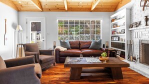 A cozy living room with a wooden ceiling, a brown leather sofa, a coffee table with chess pieces, and a fireplace. - Sauna, Lake Views + Firepits | Near Lake Arrowhead Village | Zurich Drive (Lake Arrowhead)