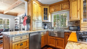 A kitchen with wooden cabinets, granite countertops, a dishwasher, a stove, and a window overlooking greenery. - Sauna, Lake Views + Firepits | Near Lake Arrowhead Village | Zurich Drive (Lake Arrowhead)