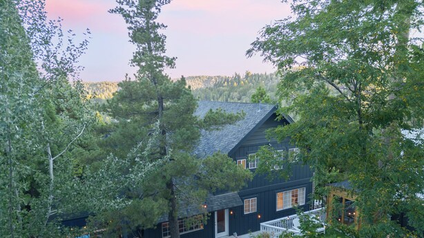 A two-story house with a dark exterior, a front porch, and a well-maintained lawn. - Sauna, Lake Views + Firepits | Near Lake Arrowhead Village | Zurich Drive (Lake Arrowhead)