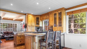 A spacious kitchen with wooden cabinets, a large island, and a view of the outdoors. - Sauna, Lake Views + Firepits | Near Lake Arrowhead Village | Zurich Drive (Lake Arrowhead)
