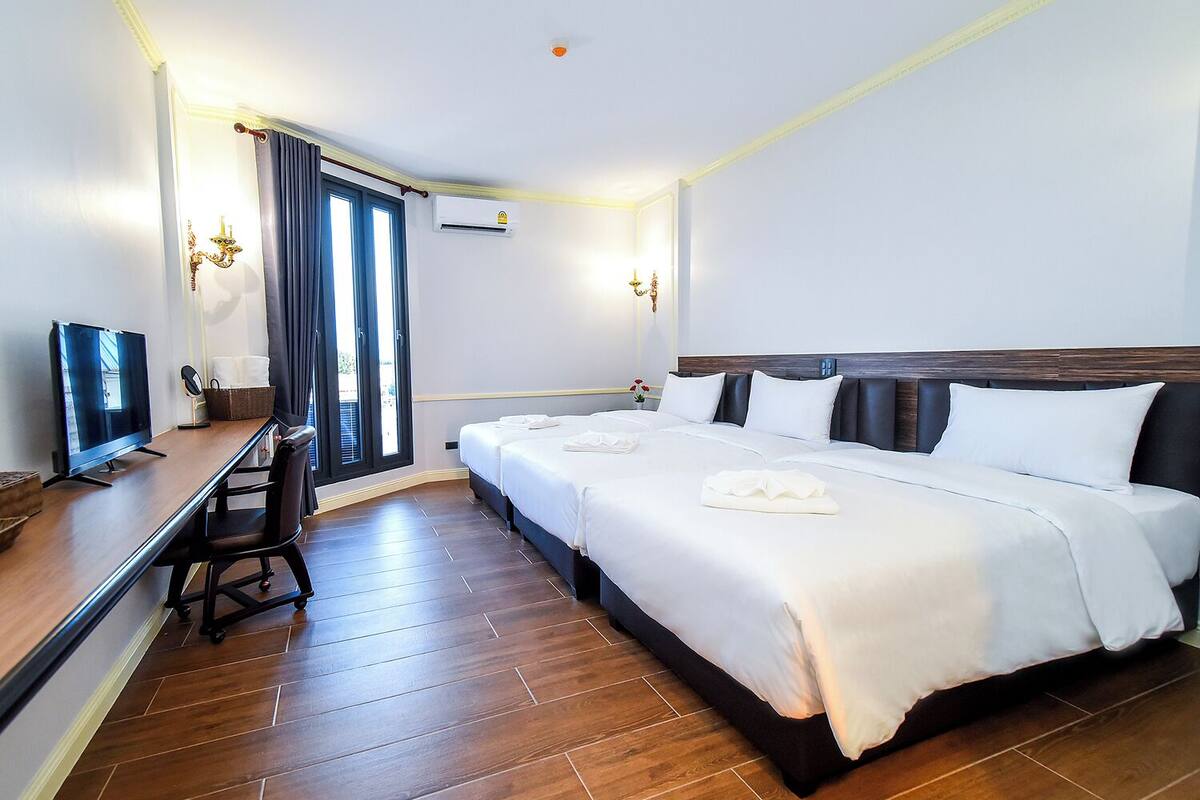 Una habitación de hotel con un escritorio de madera, un televisor de pantalla plana, una cama con sábanas blancas y un ventanal grande con cortinas.