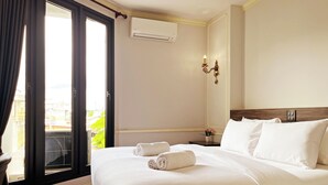 A hotel room with a bed, a nightstand, a wall-mounted air conditioner, a window with curtains, and a view of the outside. - The MACEO Hotel (Nong Khai)