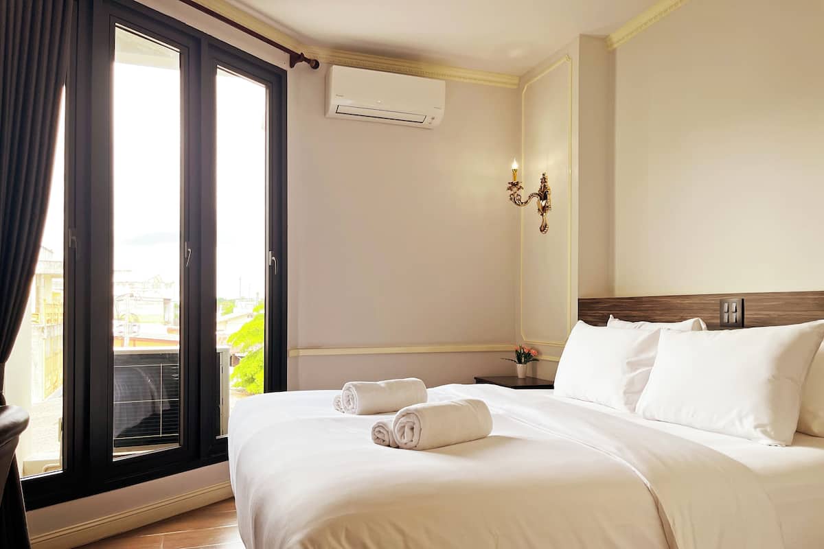 Habitación de hotel con cama, mesita de noche, aire acondicionado instalado en la pared, ventana con cortinas y vista al exterior.