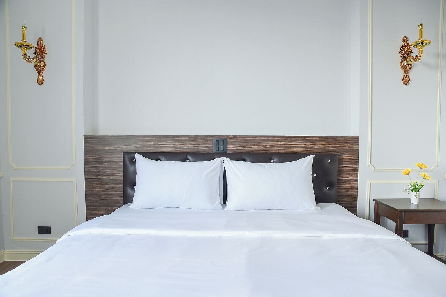 A neatly made bed with a wooden headboard, two bedside tables with lamps, and a small vase with flowers on one table.