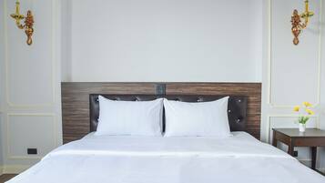 A neatly made bed with a wooden headboard, two bedside tables with lamps, and a small vase with flowers on one table.
