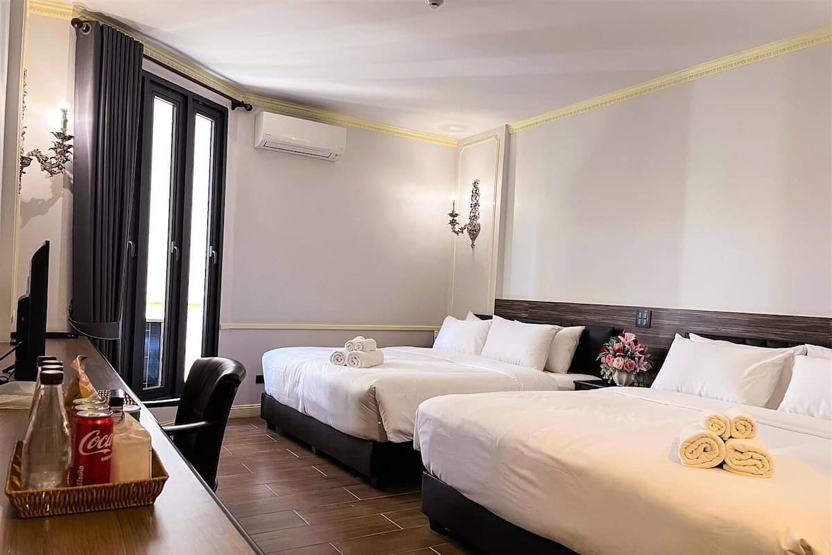 Una habitación de hotel con dos camas, un escritorio con una botella de Coca-Cola, una silla y un ventanal con cortinas.