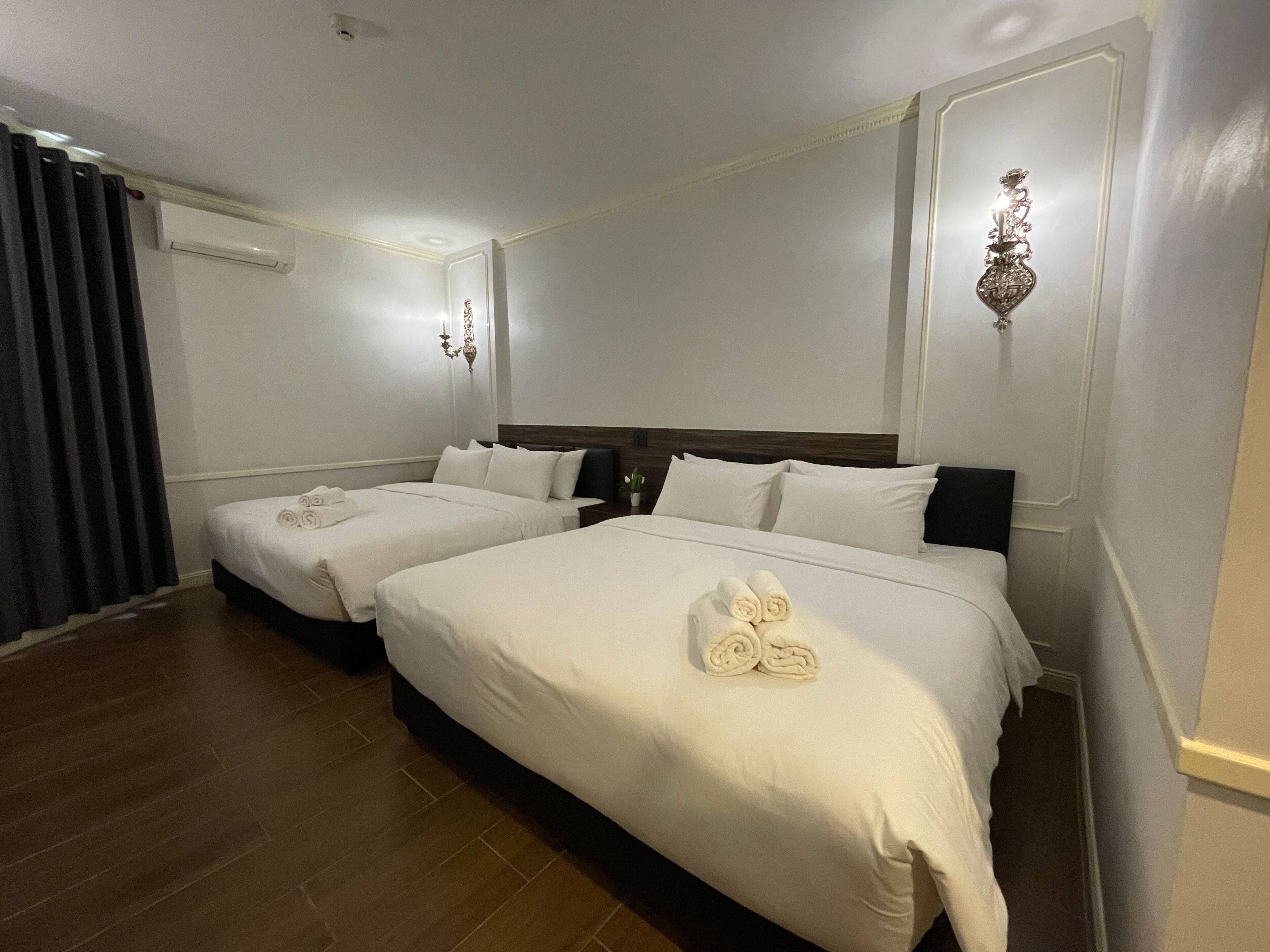 Een hotelkamer met twee bedden, een donker gordijn, een airconditioning en een wandlamp.