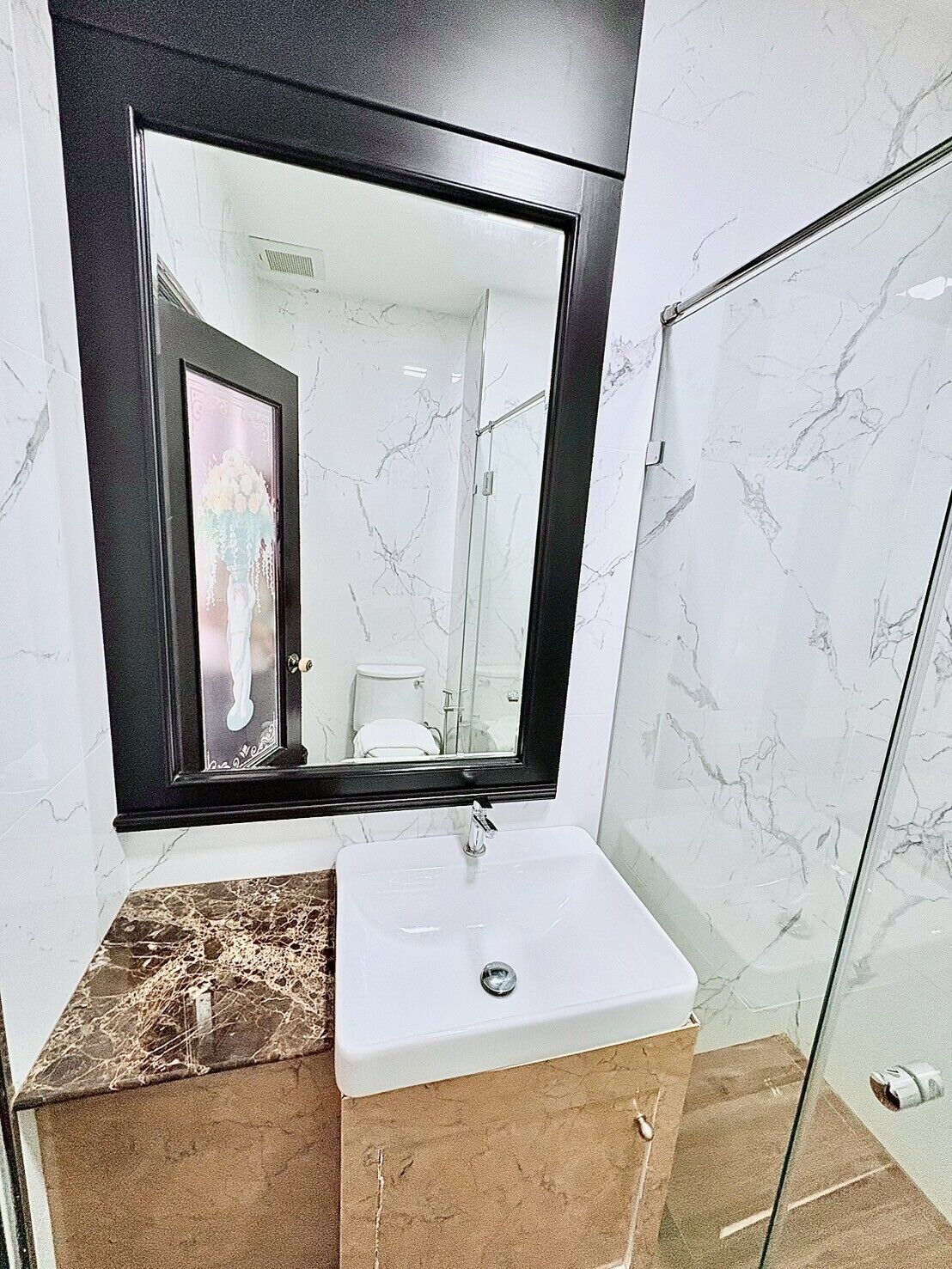 Un baño con lavamanos blanco, un espejo grande y una zona de ducha.