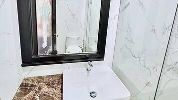 Un baño con lavamanos blanco, un espejo grande y una zona de ducha.