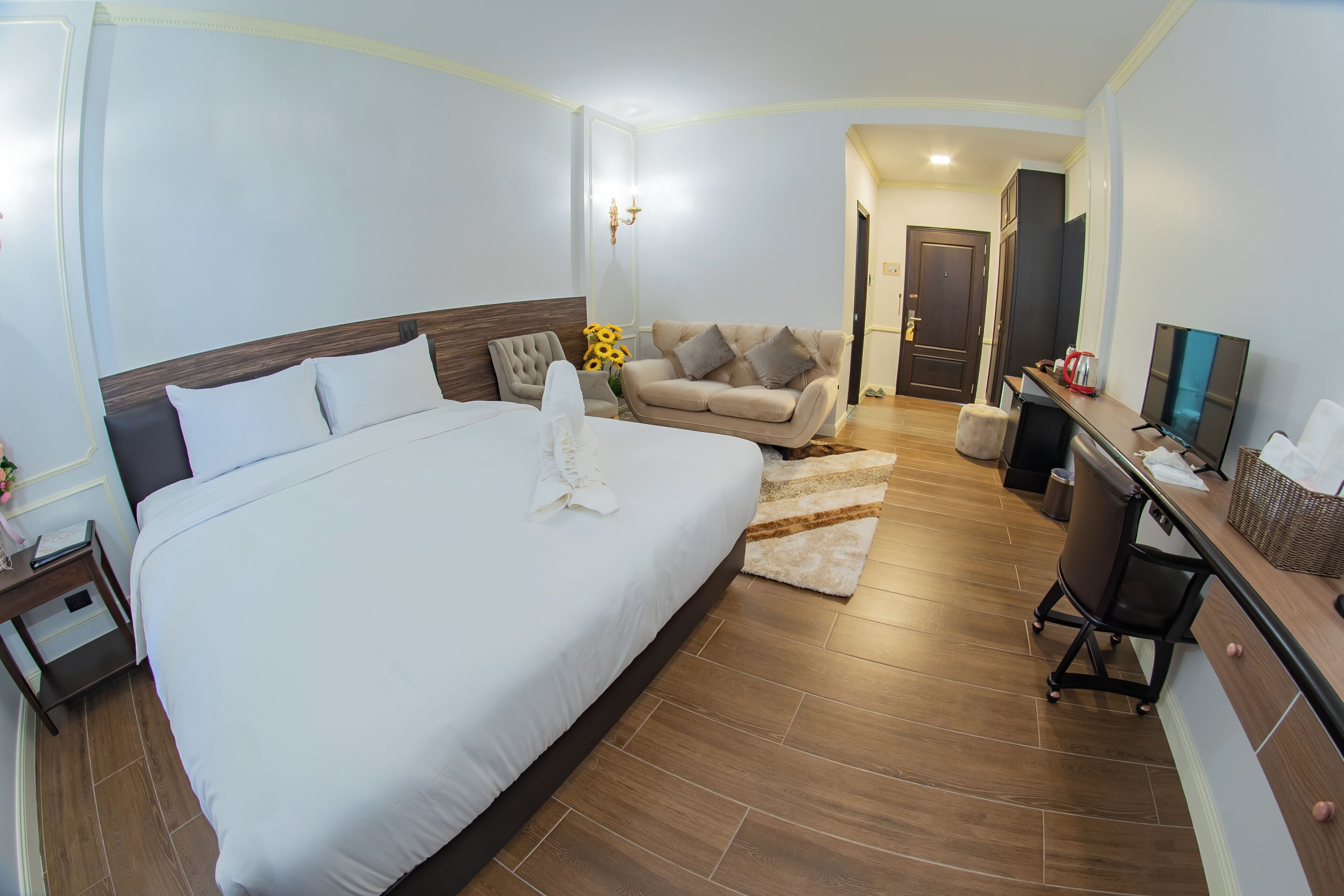 A hotel room with a large bed, a sofa, a desk with a computer, and a TV.
