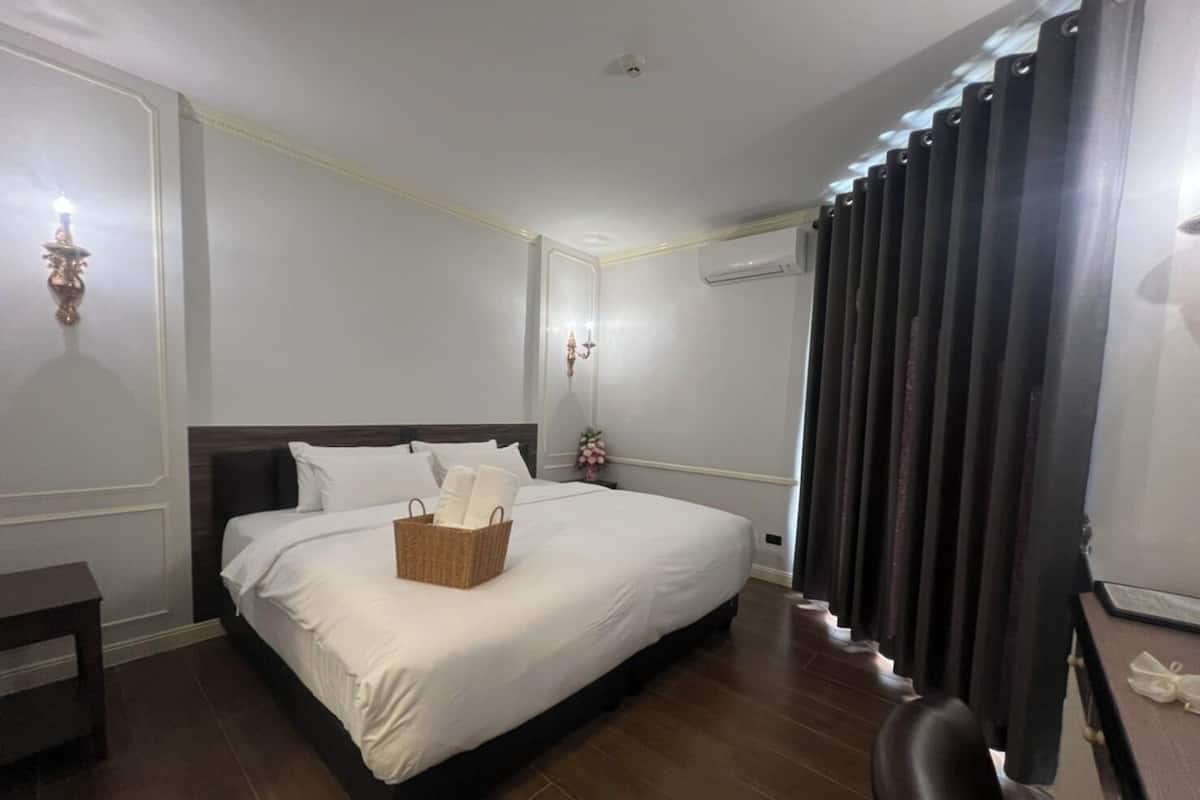 Habitación de hotel con una cama grande, una mesita de noche, una lámpara y una ventana con cortinas.