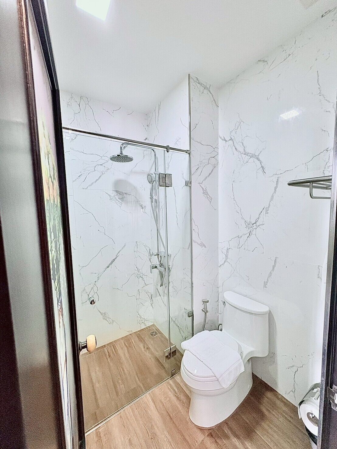 Un baño con ducha de mampara de vidrio, inodoro y paredes de mármol.