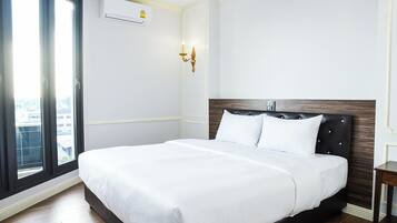 A hotel room with a large bed, a window with blinds, an air conditioning unit, and a wall-mounted light fixture.