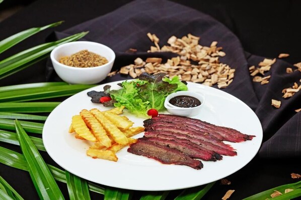 Une assiette garnie de viande tranchée, de frites, de salade et de deux petits ramequins de condiments.
